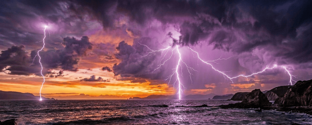 Lightning striking the ocean beneath dark storm clouds at sunset